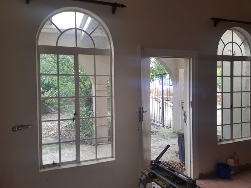 An empty living area featuring arched windows and a door leading to an outdoor patio space, with neutral walls and tiled flooring.