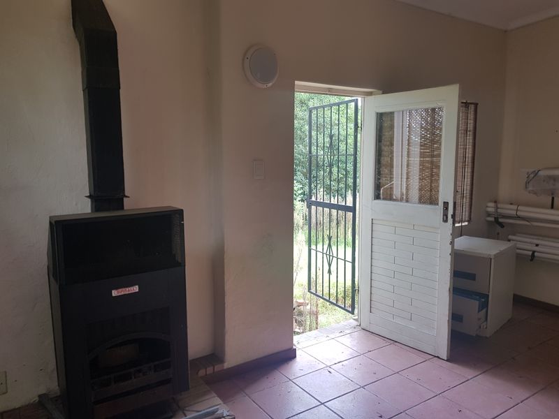 An empty living area featuring a black freestanding fireplace, tiled flooring, and direct access to the exterior through a security gate and door.
