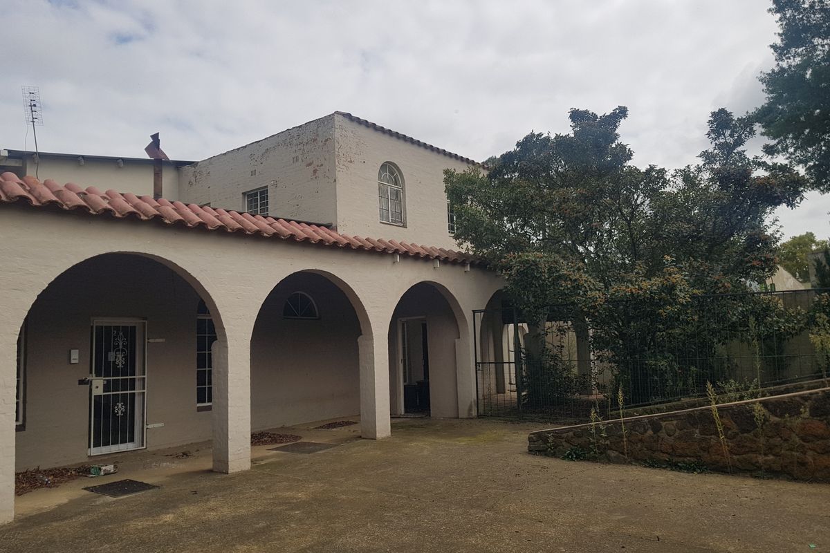 Rear exterior view of a commercial building featuring a covered arched walkway, terracotta roof tiles, and a paved courtyard area.