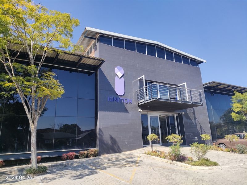 Modern industrial office building featuring a dark tiled facade, extensive glass curtain walling, and a prominent upper-level balcony entrance.