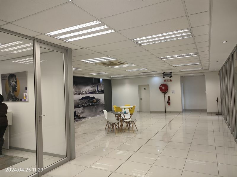 Spacious open-plan office area featuring tiled flooring, suspended ceilings with recessed lighting, and glass partition walls, suitable for a professional workspace.