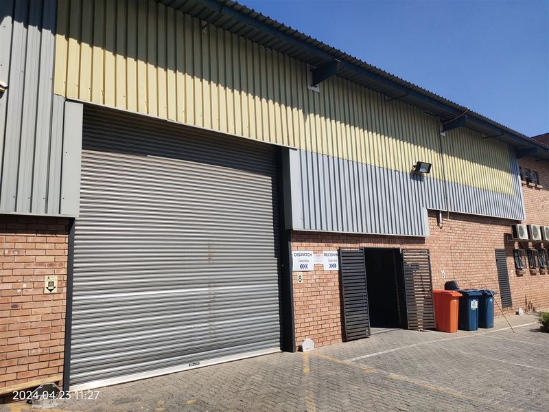 Industrial warehouse exterior featuring a large roller shutter door, brick and metal cladding facade, and paved access area for dispatch and receiving.