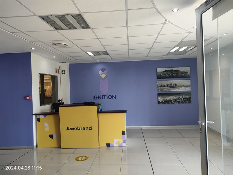 A professional office reception area featuring a branded front desk, tiled flooring, and a suspended ceiling with integrated lighting.