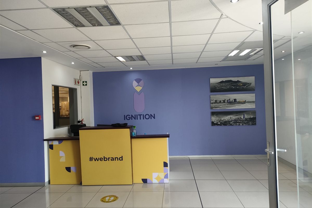 A professional office reception area featuring a branded front desk, tiled flooring, and a suspended ceiling with integrated lighting.