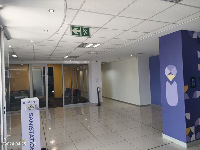 A clean, modern industrial hallway featuring tiled flooring, suspended ceiling with integrated lighting, and glass partition walls leading to office spaces.