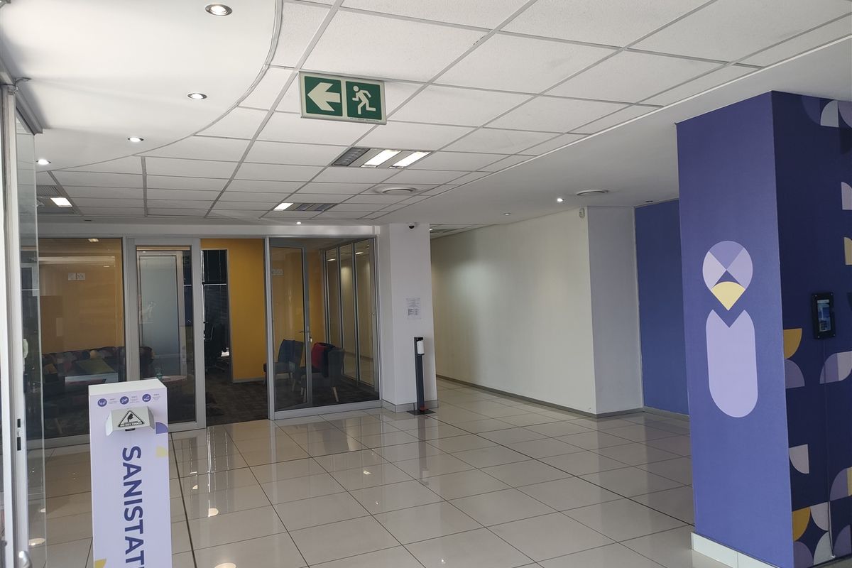 A clean, modern industrial hallway featuring tiled flooring, suspended ceiling with integrated lighting, and glass partition walls leading to office spaces.