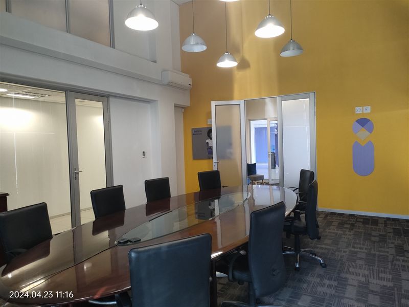 A professional office boardroom featuring high ceilings, vibrant yellow accent walls, glass partitions, and modern pendant lighting, creating a bright and functional workspace.