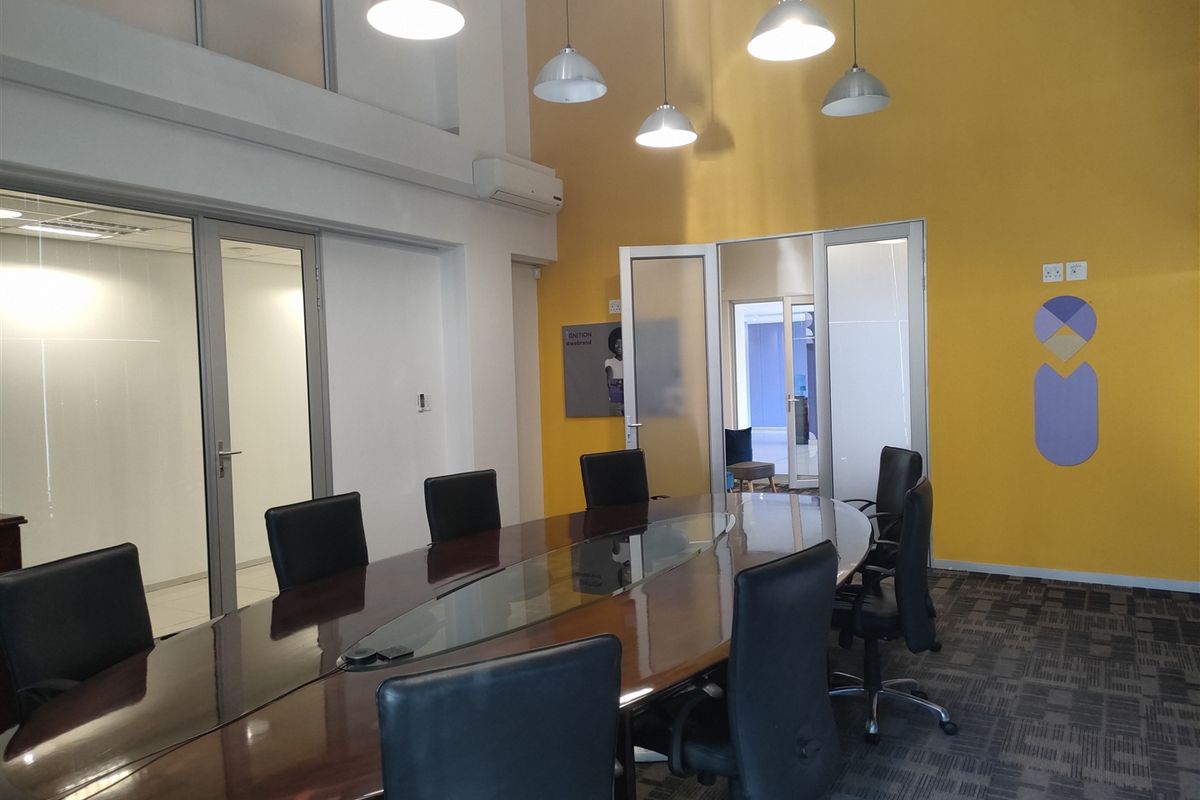 A professional office boardroom featuring high ceilings, vibrant yellow accent walls, glass partitions, and modern pendant lighting, creating a bright and functional workspace.