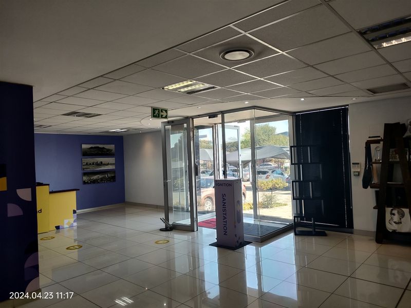 A bright and spacious industrial office entrance featuring tiled flooring, a suspended ceiling with recessed lighting, and glass double doors leading to the exterior.