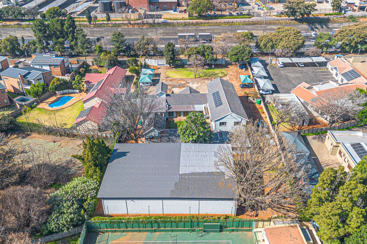 Aerial view of a commercial property featuring a large warehouse structure, tennis court, paved parking with shade ports, and surrounding landscaped grounds.