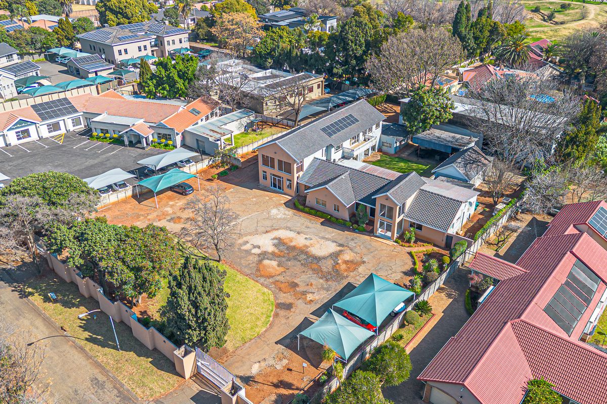 Aerial view of a commercial property complex featuring multiple buildings, paved parking areas with shade cloth carports, and established garden surroundings.