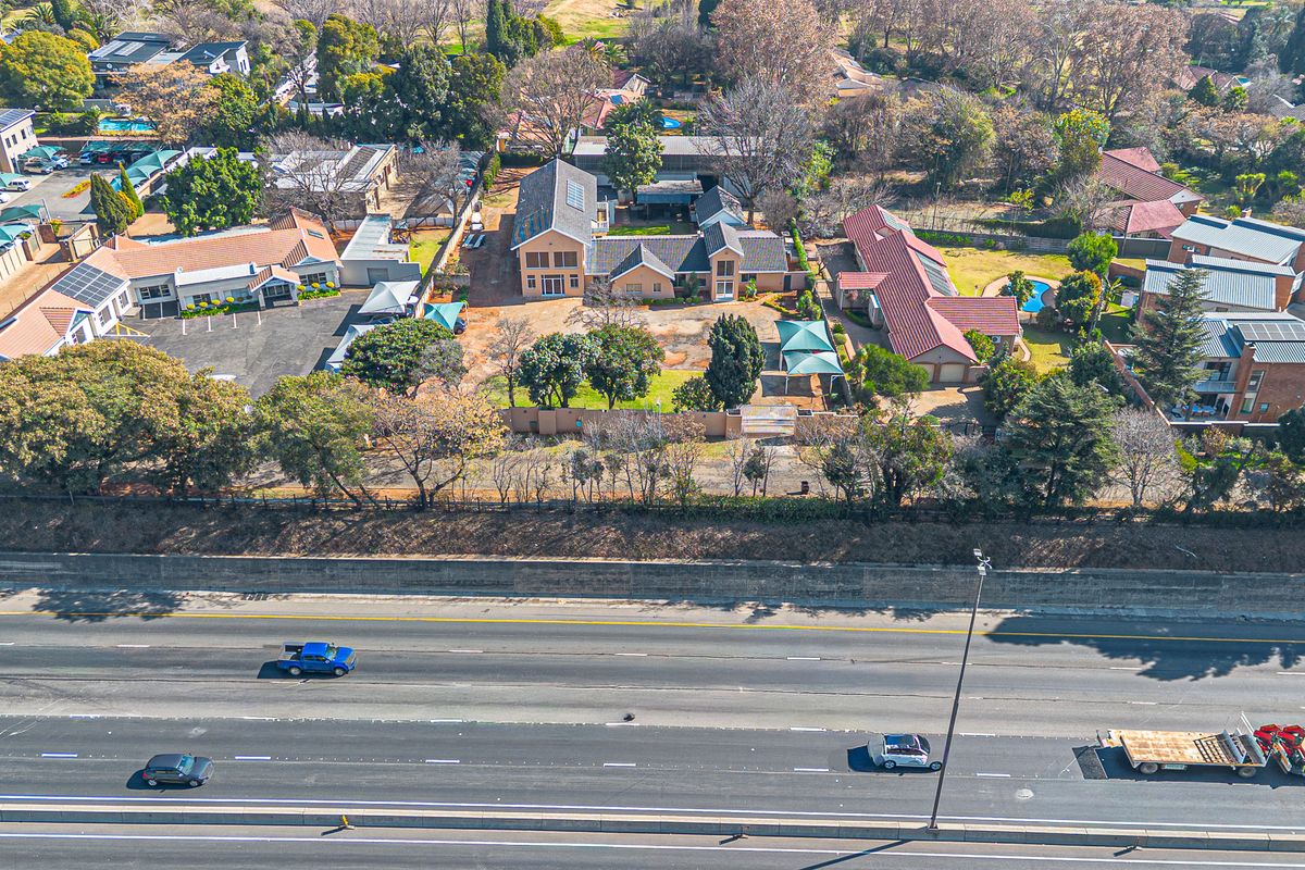 Aerial view of a commercial property complex featuring multiple buildings, paved parking areas, and a swimming pool, situated adjacent to a major highway.