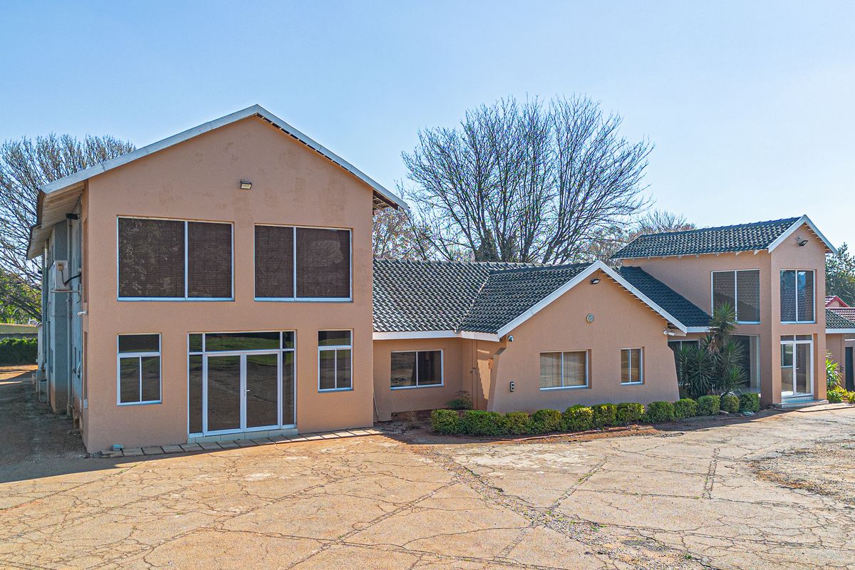 Rear view of a multi-level commercial building featuring a tiled roof, plastered facade, and extensive paved driveway area.