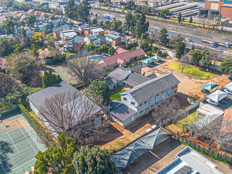 Aerial view of a commercial property complex featuring a tennis court, swimming pool, extensive parking with shade cloth carports, and multiple building structures.