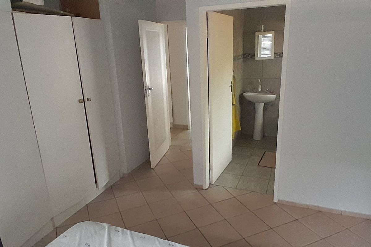 A bedroom featuring built-in cupboards, tiled flooring, and direct access to an en-suite bathroom with a pedestal basin.