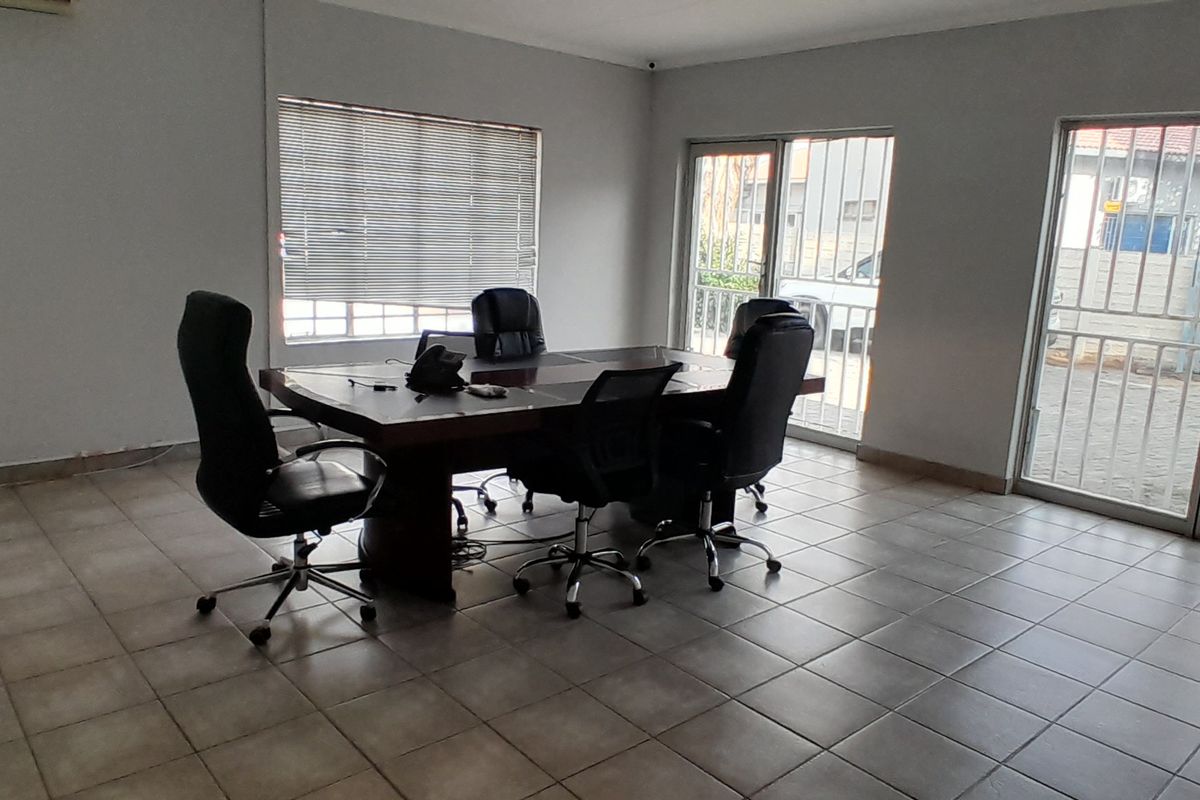 A functional office space featuring tiled flooring, large windows with blinds, and secure sliding glass door access to the exterior.