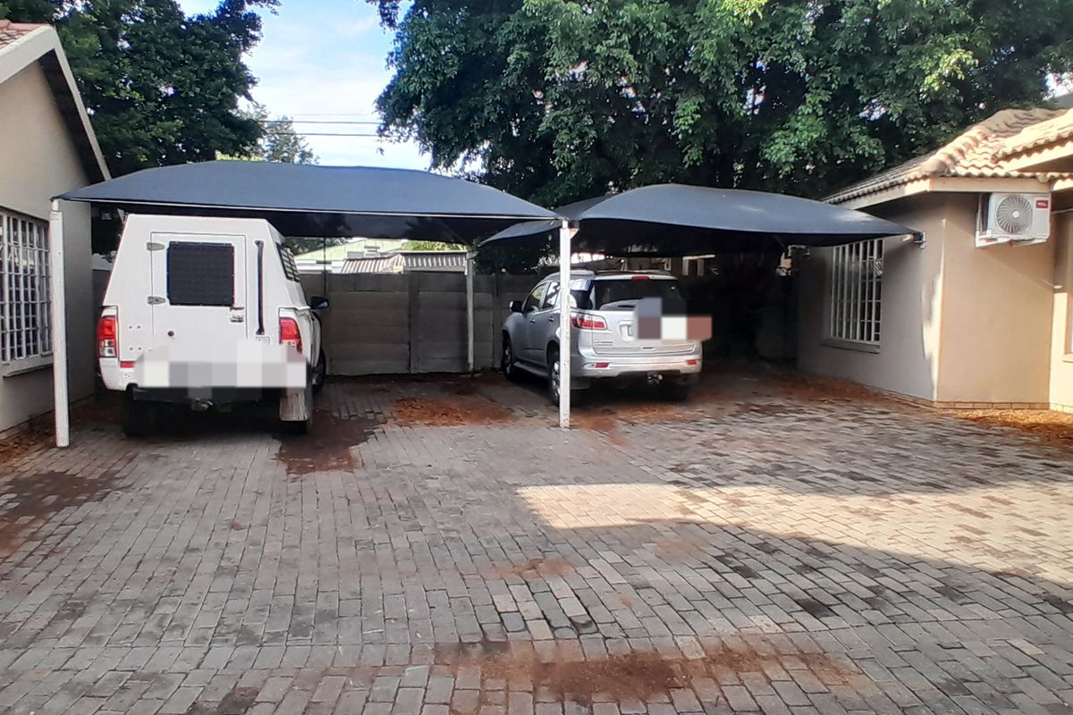 Exterior view of a paved parking area featuring a double shade cloth carport, security bars on windows, and an external air conditioning unit.