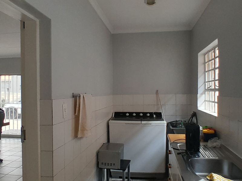 A functional laundry area featuring a stainless steel sink, tiled splashback, and security bars on the windows, with an adjacent office space visible.