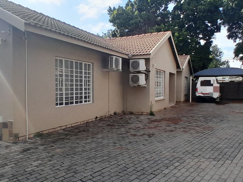 Exterior view of the property featuring a paved driveway, tiled roof, security bars on windows, multiple air conditioning units, and a covered carport area.
