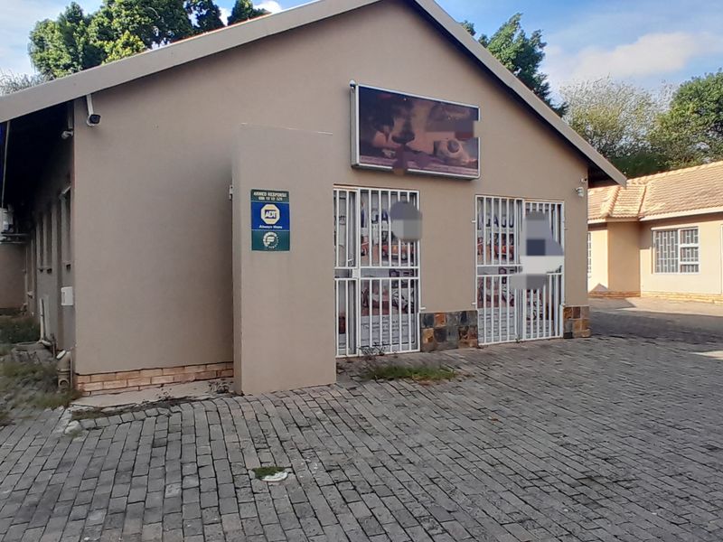 Front exterior view of a commercial property featuring a paved driveway, security gates, and external signage.