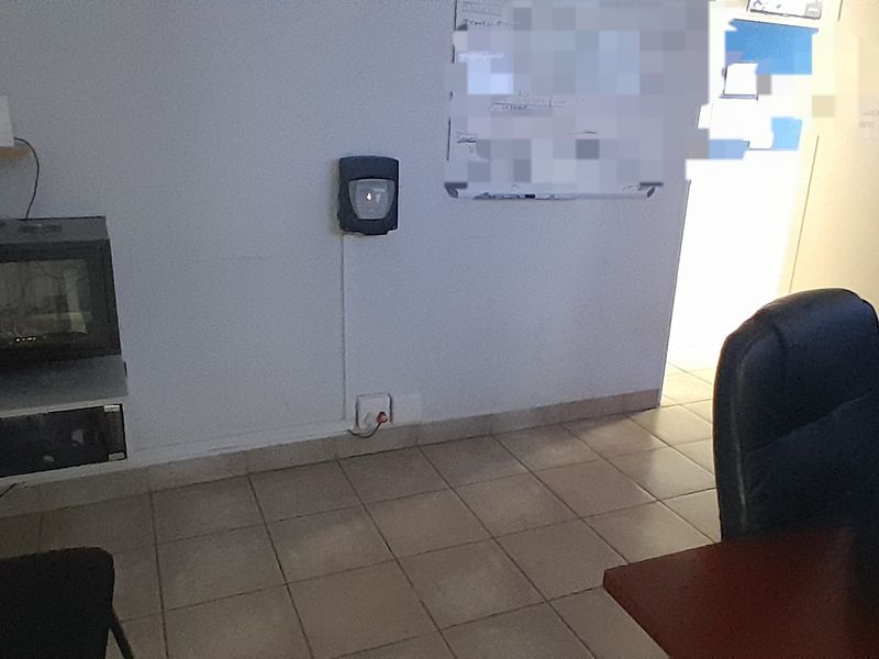 A functional office space featuring tiled flooring and wall-mounted infrastructure including a server rack and security system.