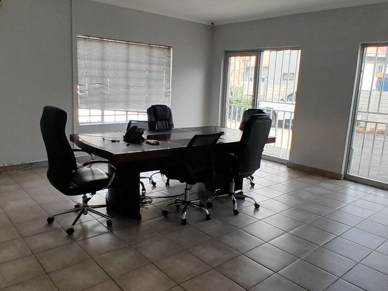 A functional office space featuring tiled flooring, large windows with blinds, and secure sliding glass door access to the exterior.