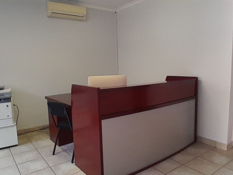 A functional office space featuring tiled flooring, a built-in reception desk, and a wall-mounted air conditioning unit.
