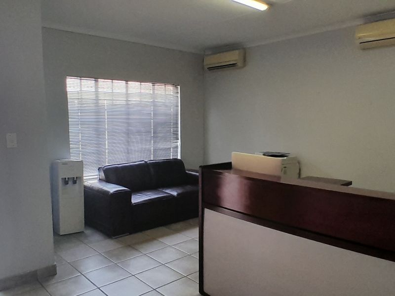 A functional office space featuring tiled flooring, dual air conditioning units, and a built-in reception counter with natural light from the window.