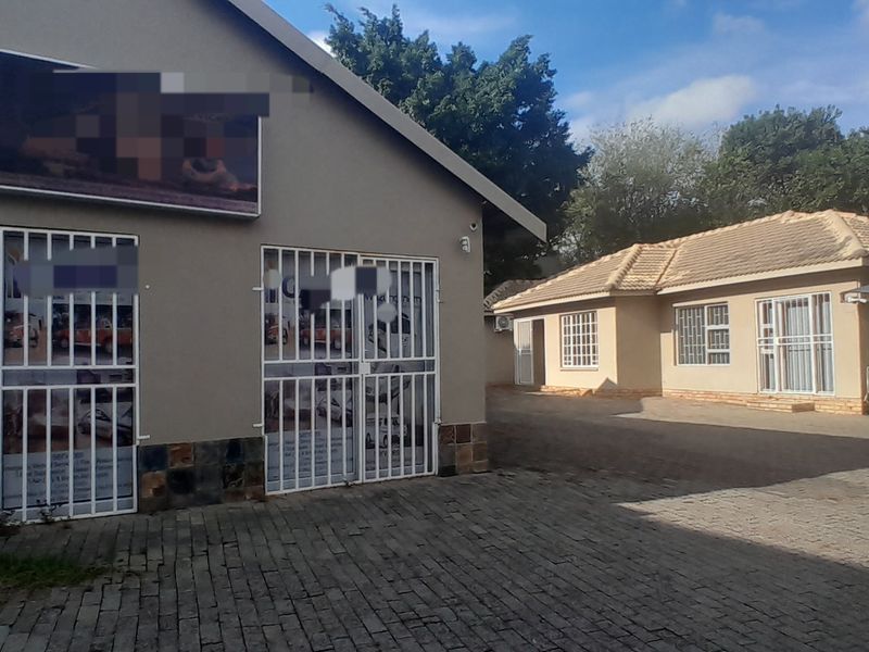 Exterior view of a business property featuring a paved driveway, security gates, and a carport area with tiled roof structures.