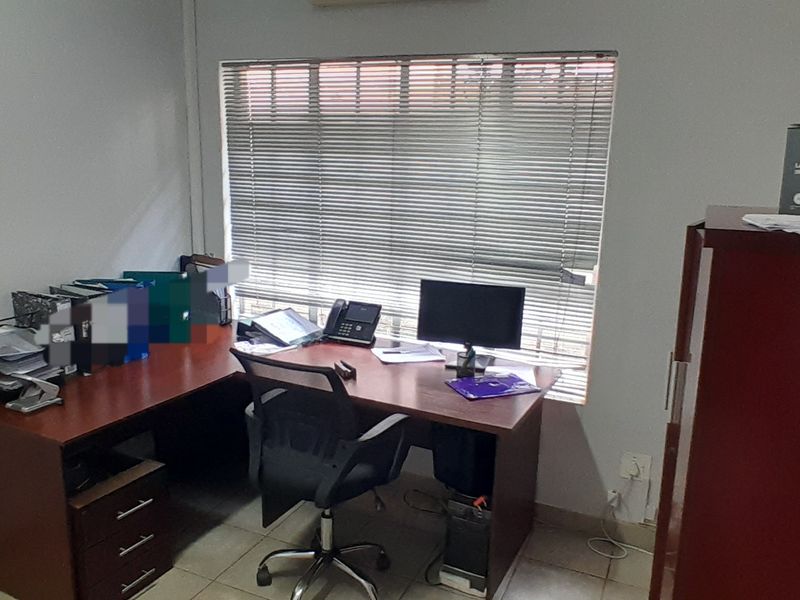 A functional office space featuring tiled flooring and a large window with fitted venetian blinds, providing natural light for a productive work environment.