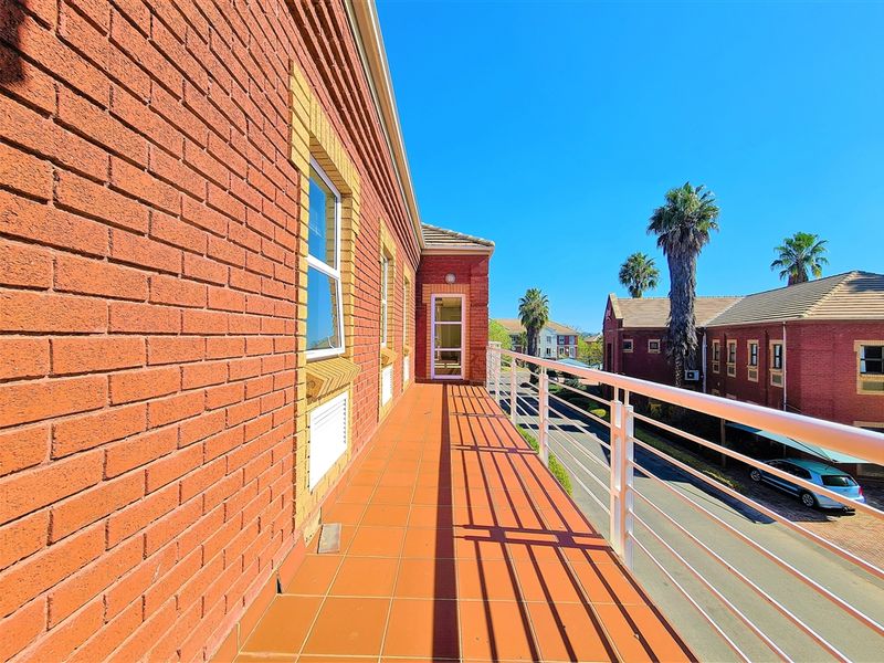 A spacious exterior balcony featuring red brick wall finishes, tiled flooring, and a white metal balustrade overlooking the street.
