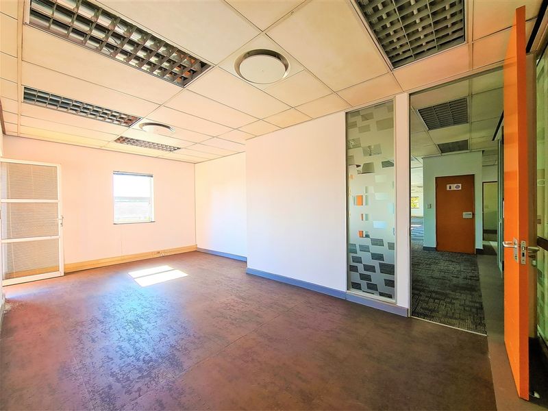 A vacant office space featuring a suspended ceiling with recessed lighting, a frosted glass partition, and durable vinyl flooring.