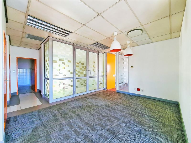 A vacant office space featuring carpeted flooring, a suspended ceiling with integrated lighting, and glass partition walls providing a professional layout.