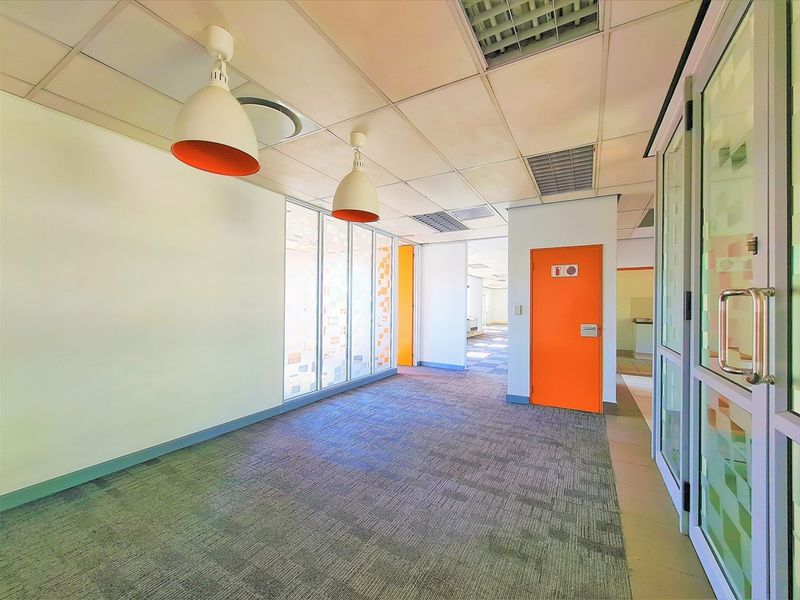 An empty office space featuring carpet tiles, suspended ceilings, glass partitions, and vibrant orange accent doors, providing a clean and functional professional environment.