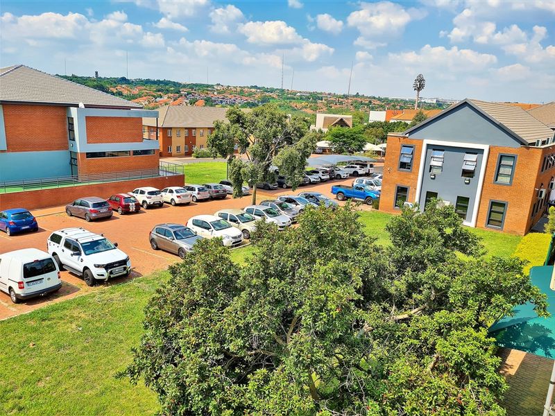 An elevated aerial view of an office park complex featuring brick buildings, paved parking areas, and surrounding landscaped grounds.