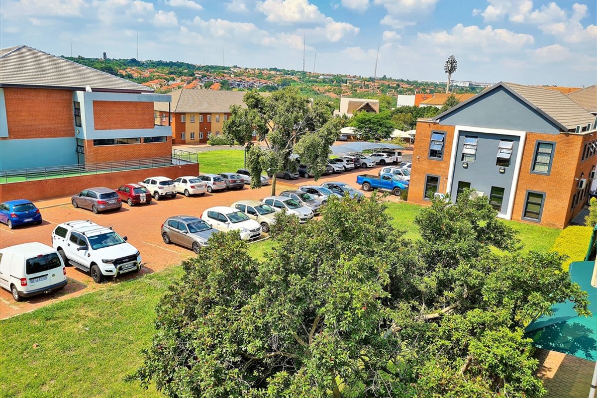 An elevated aerial view of an office park complex featuring brick buildings, paved parking areas, and surrounding landscaped grounds.