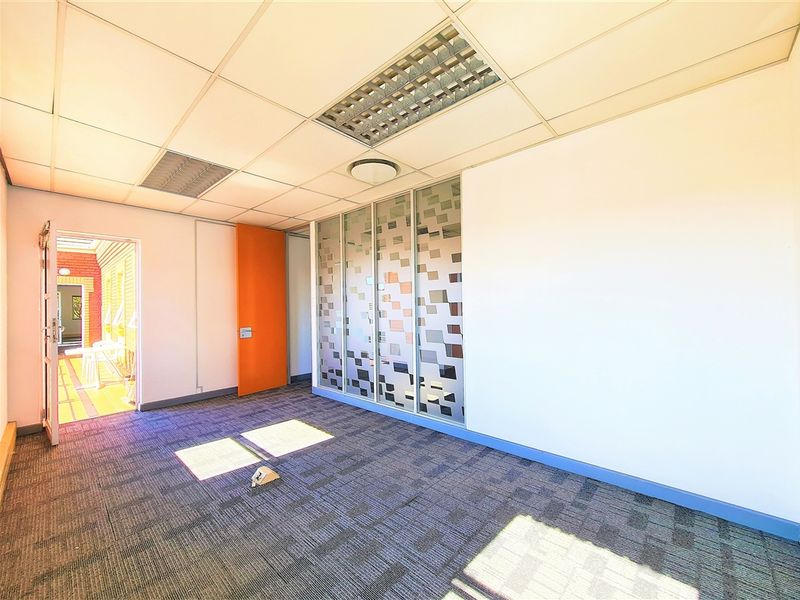 A vacant office space featuring carpet tiles, a suspended ceiling with recessed lighting, and a modern frosted glass partition wall.