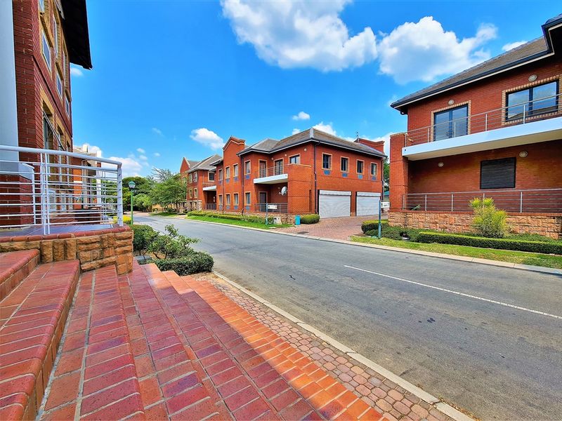 A street-level view of a modern office complex featuring red brick architecture, paved access roads, and integrated garage facilities.