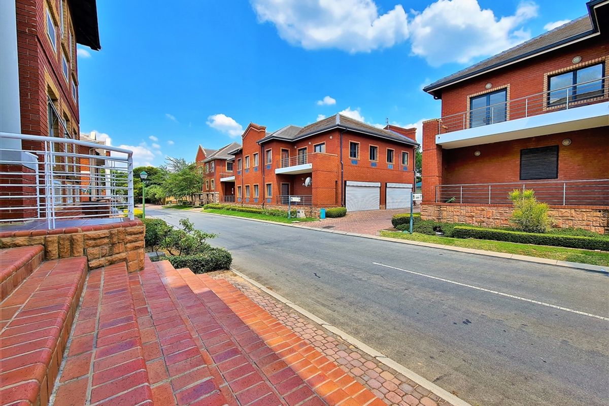 A street-level view of a modern office complex featuring red brick architecture, paved access roads, and integrated garage facilities.