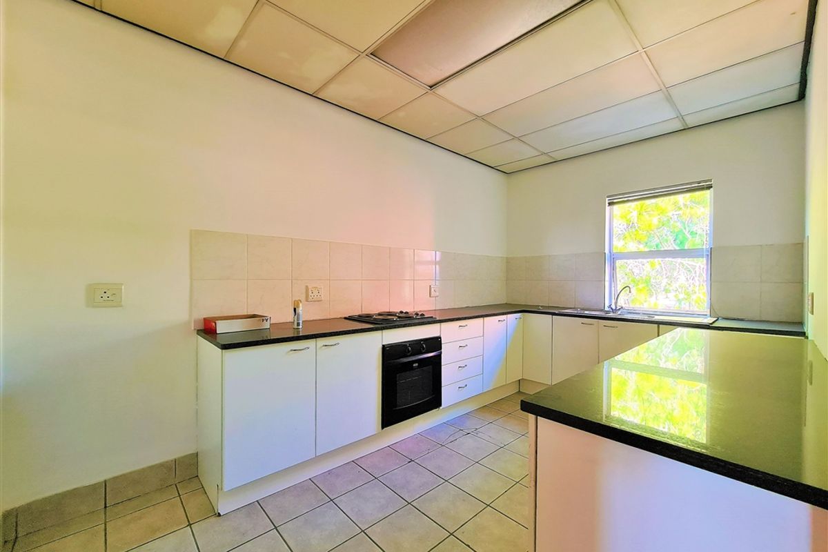 A functional office kitchen featuring granite countertops, built-in oven, gas hob, and tiled flooring, offering a clean and practical workspace.
