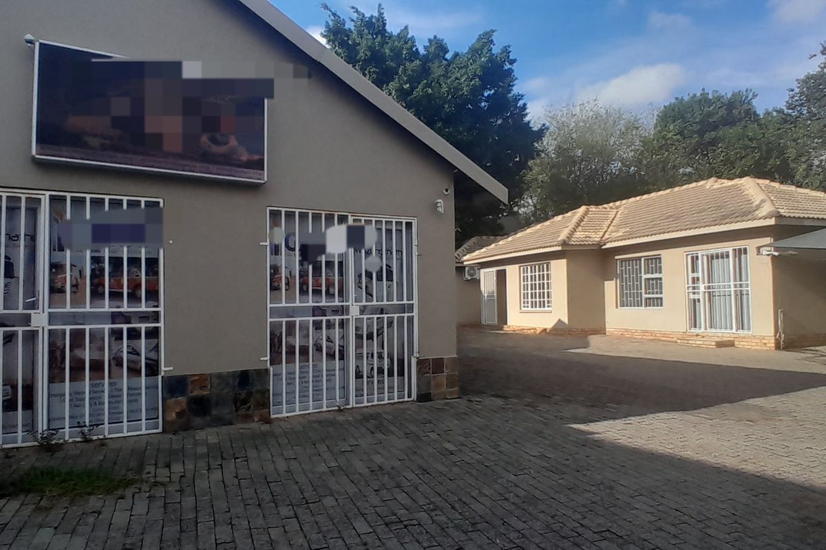 Exterior view of a business property featuring a paved driveway, security gates, and a carport area with tiled roof structures.