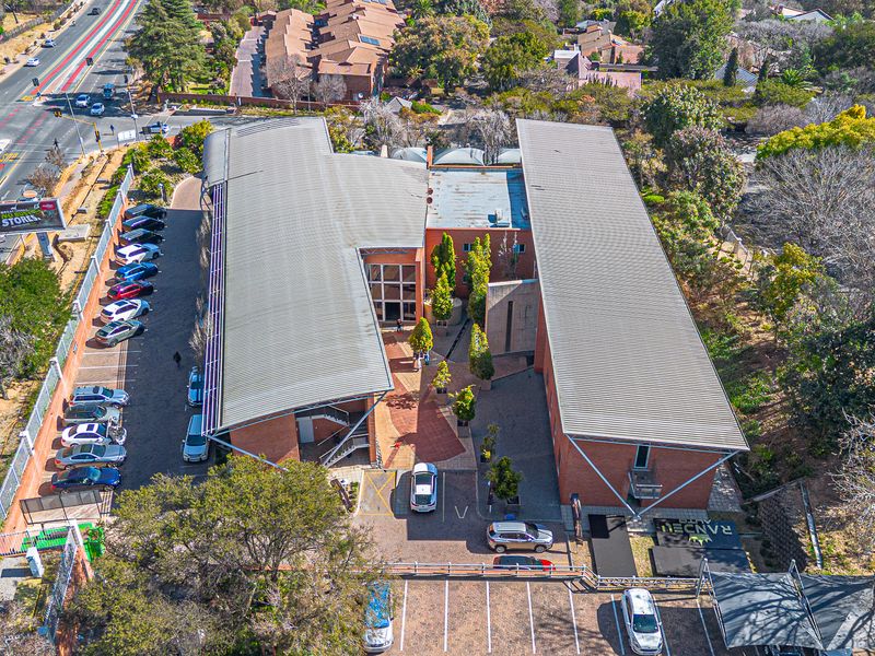 Aerial view of a modern office complex featuring brick architecture, metal roofing, extensive paved parking, and a central landscaped courtyard.