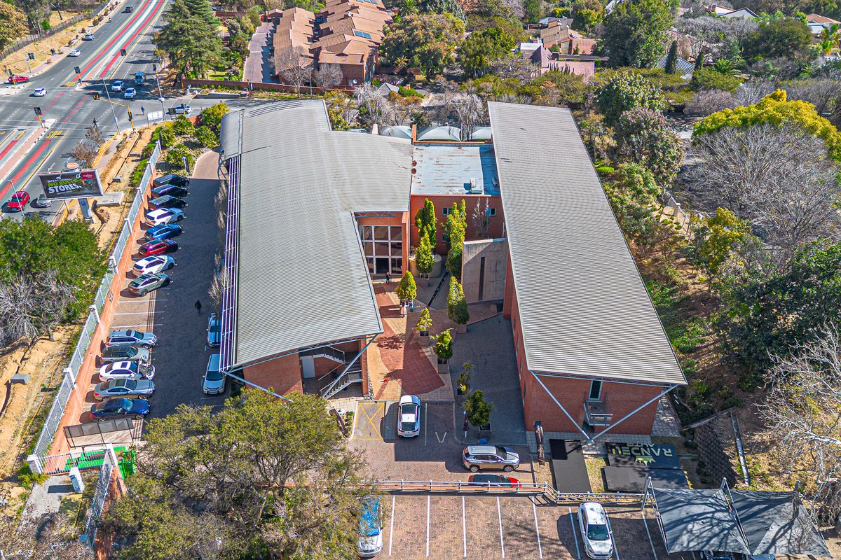 Aerial view of a modern office complex featuring brick architecture, metal roofing, extensive paved parking, and a central landscaped courtyard.