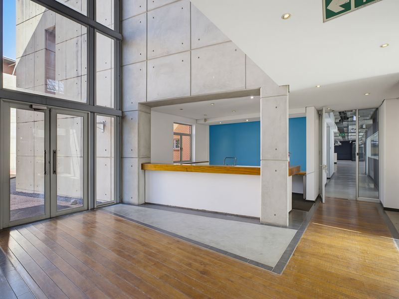 Modern office entrance lobby featuring double-height glass windows, exposed concrete architectural elements, and a built-in reception counter with timber detailing.