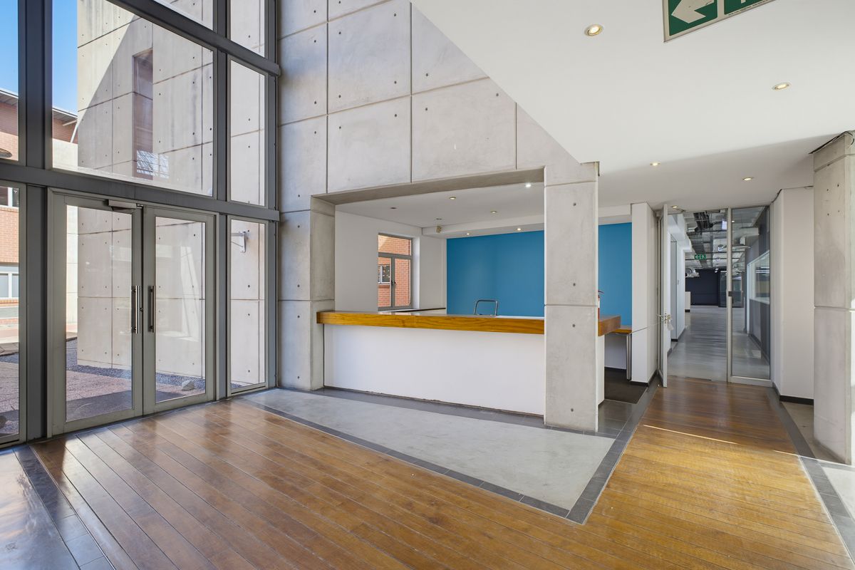 Modern office entrance lobby featuring double-height glass windows, exposed concrete architectural elements, and a built-in reception counter with timber detailing.