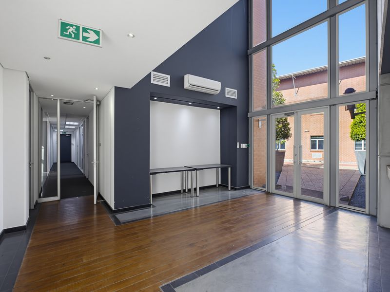 Modern office entrance featuring double-height glass windows, polished concrete and timber flooring, and a split-system air conditioner.