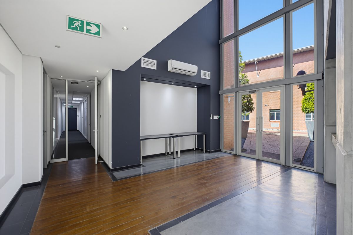 Modern office entrance featuring double-height glass windows, polished concrete and timber flooring, and a split-system air conditioner.