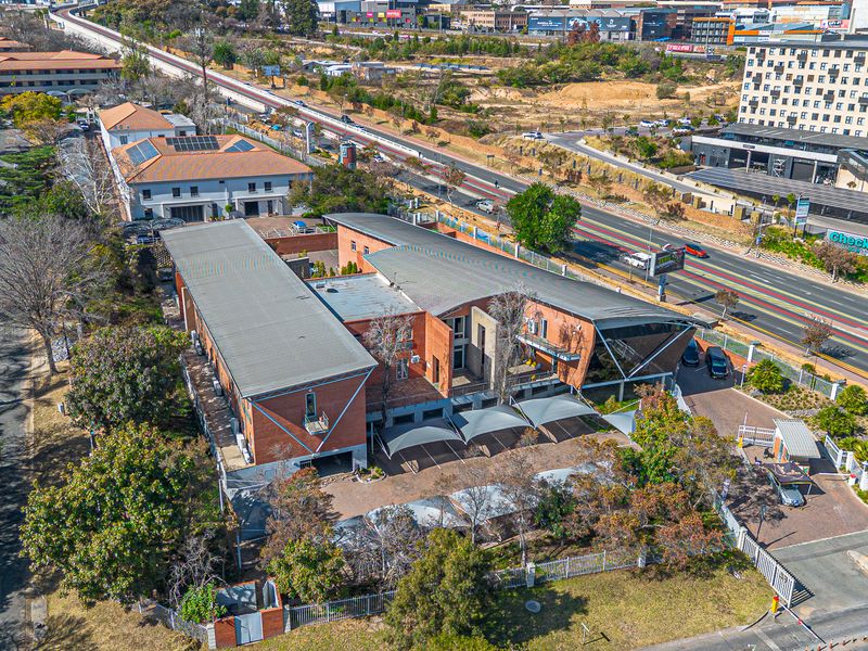 Aerial view of a modern office complex featuring brick architecture, metal roofing, solar panels, and a paved parking area with shade cloth carports.