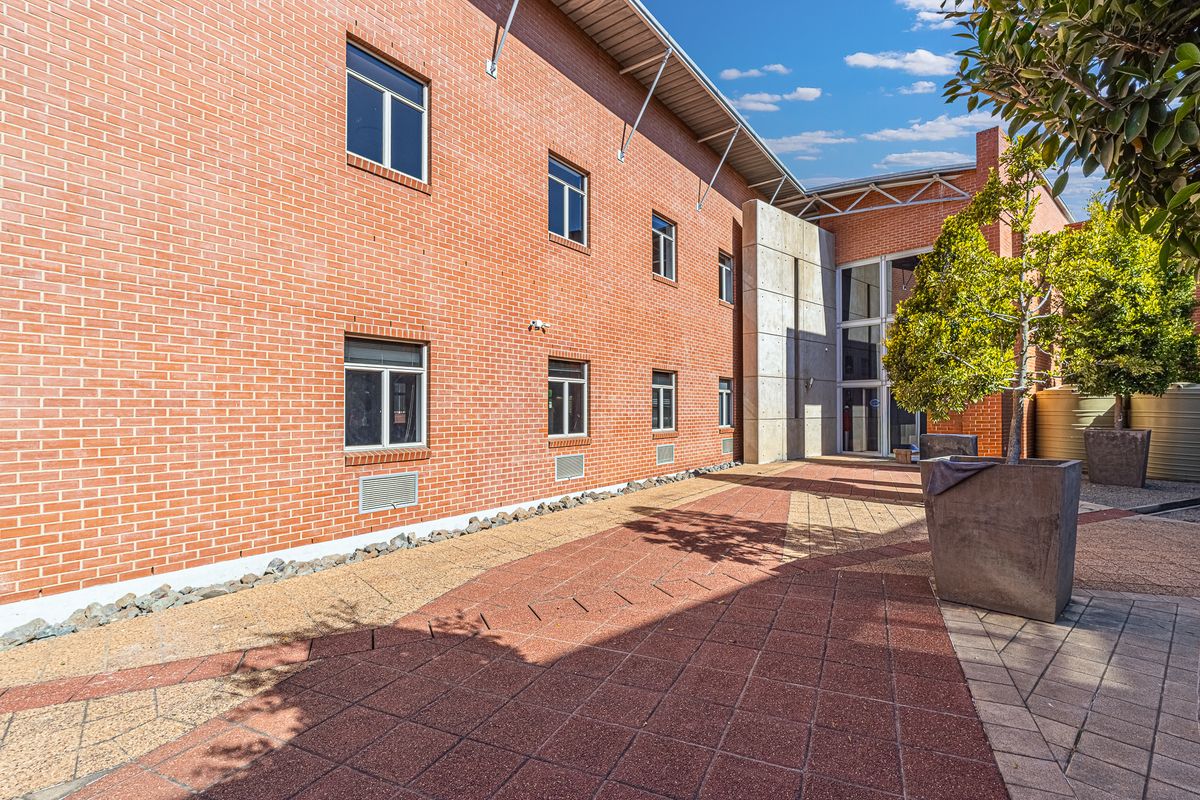 A well-maintained rear courtyard featuring exposed brickwork, a modern concrete accent wall, and paved outdoor space suitable for office break areas.