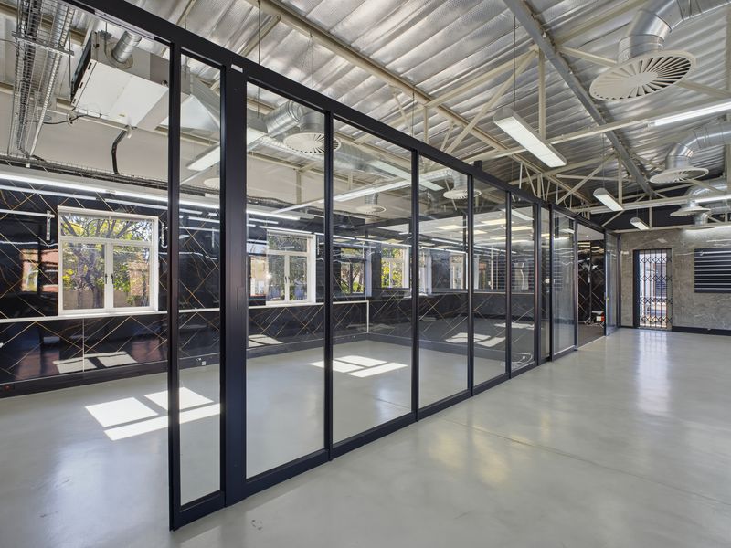 Modern open-plan office space featuring high exposed ceilings, polished epoxy flooring, and sleek glass partitions, offering a bright and professional work environment.